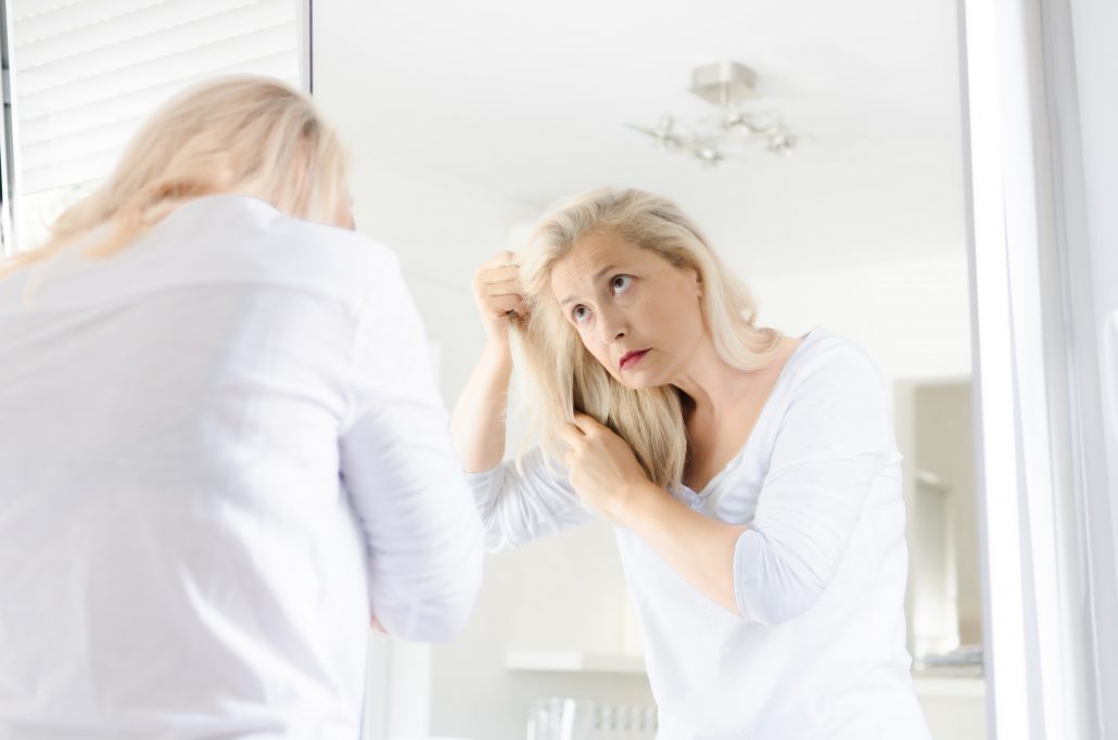 Ältere Frau leidet an Spliss und Haarbruch und begutachtet ihre Haare im Spiegel