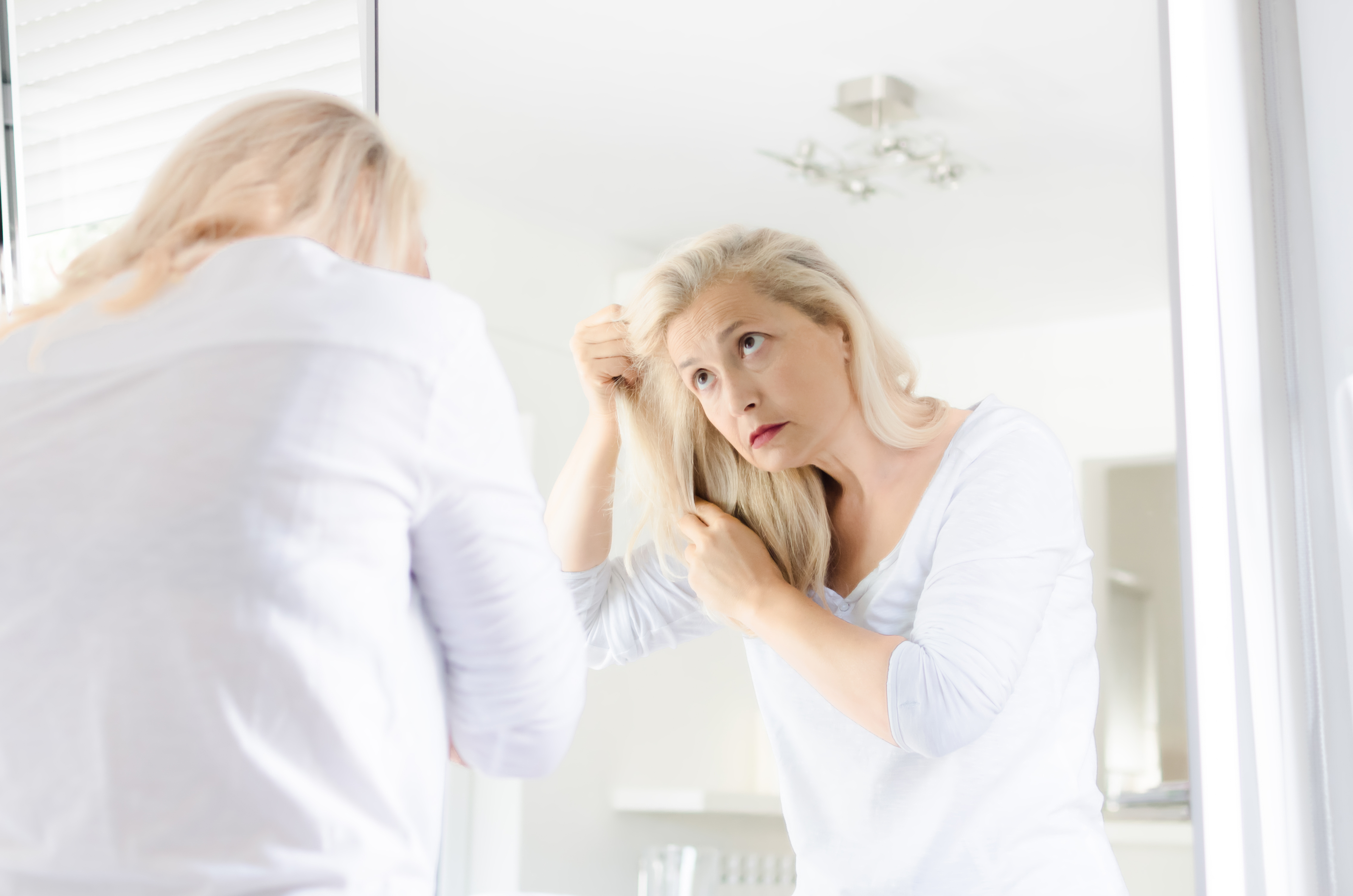 Ältere Frau leidet an Spliss und Haarbruch und begutachtet ihre Haare im Spiegel