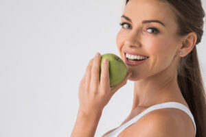 junge Frau mit Glatter Haut dank Unike Anti-Aging-Kapseln möchte in einen Apfel beißen