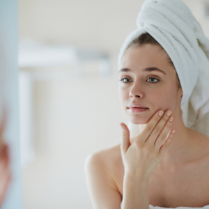 Junge Frau betrachtet sich nach dem Duschen im Spiegel und streicht sich über ihre glatte Haut dank Unike® Anti Aging Kapseln